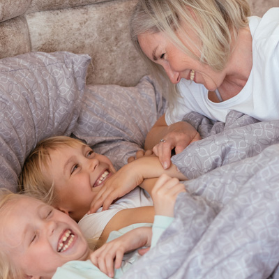 Foto van een lachende moeder die haar kinderen in bed stopt